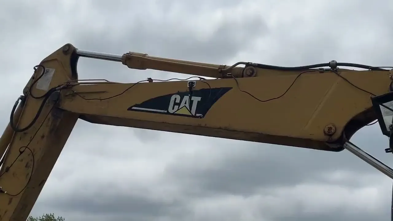 Koparka CAT na placu budowy, w tle pomiar tyczką GPS