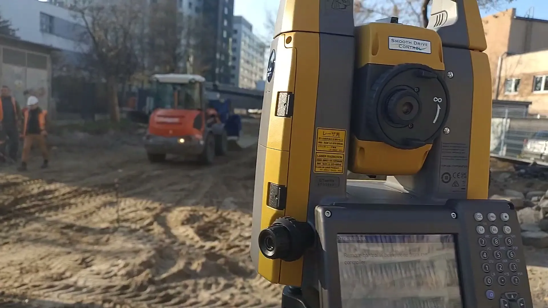 Tachimetr Topcon na placu budowy, w tle ładowarka