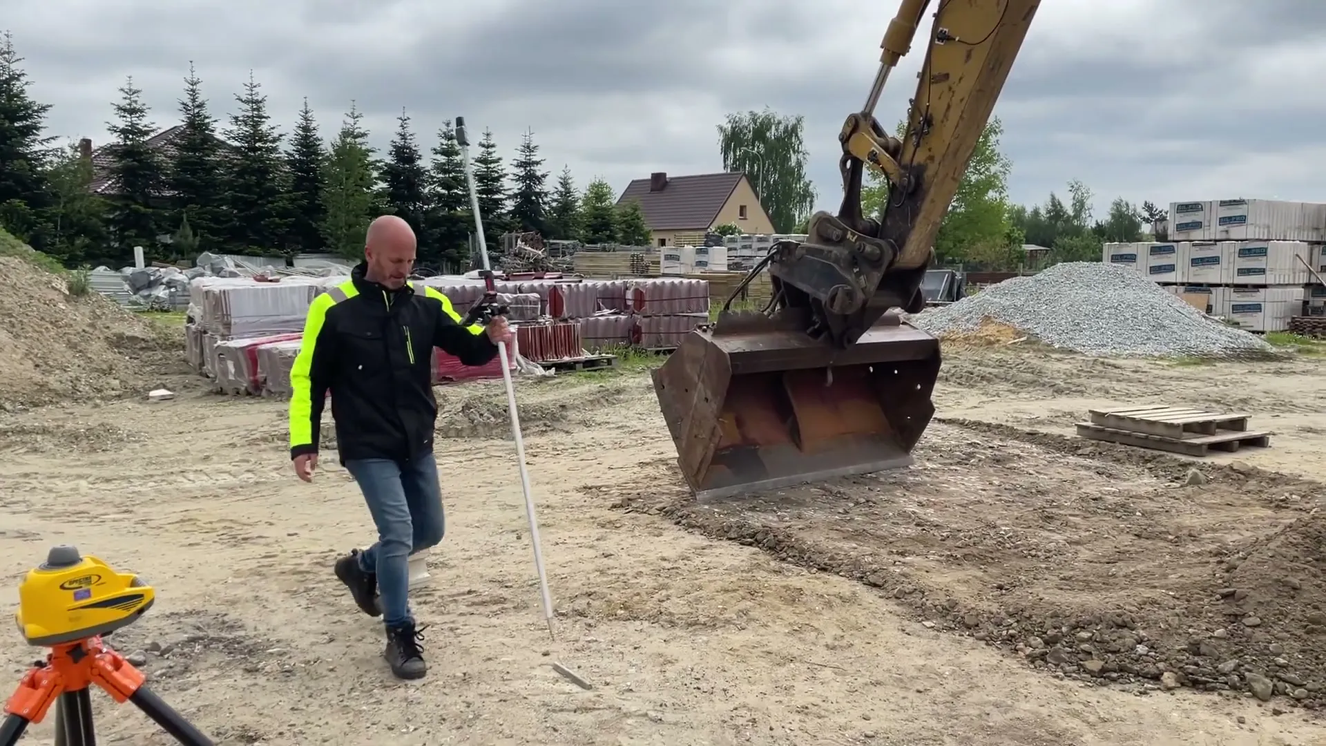 Pomiar tyczką GPS na placu budowy obok koparki